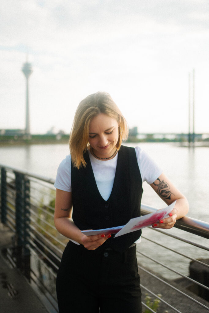 Dame lehnt lässig am Rheinufer vor Düsseldorfskyline