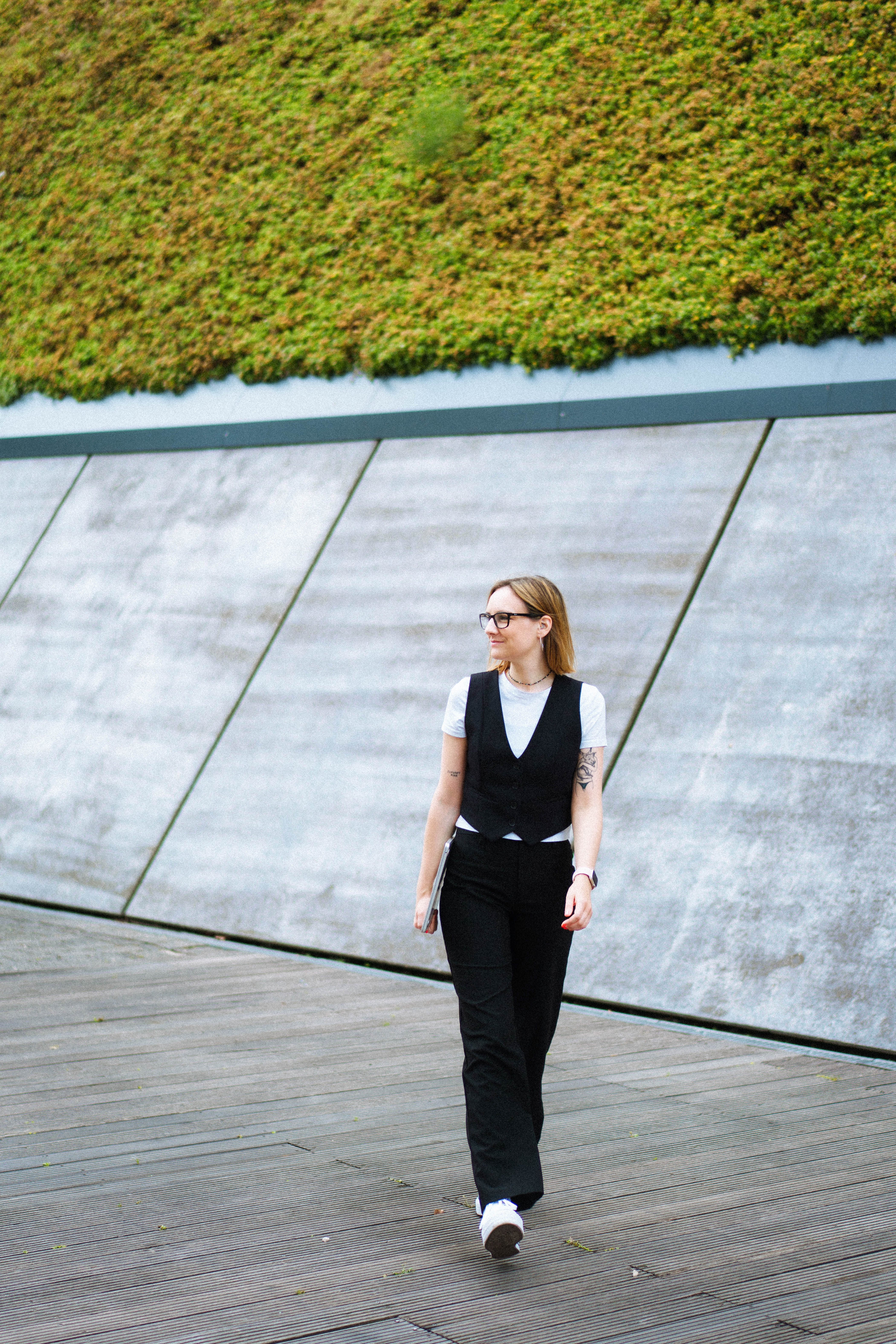 Dame läuft mit Laptop in der Hand vor grüner Wand